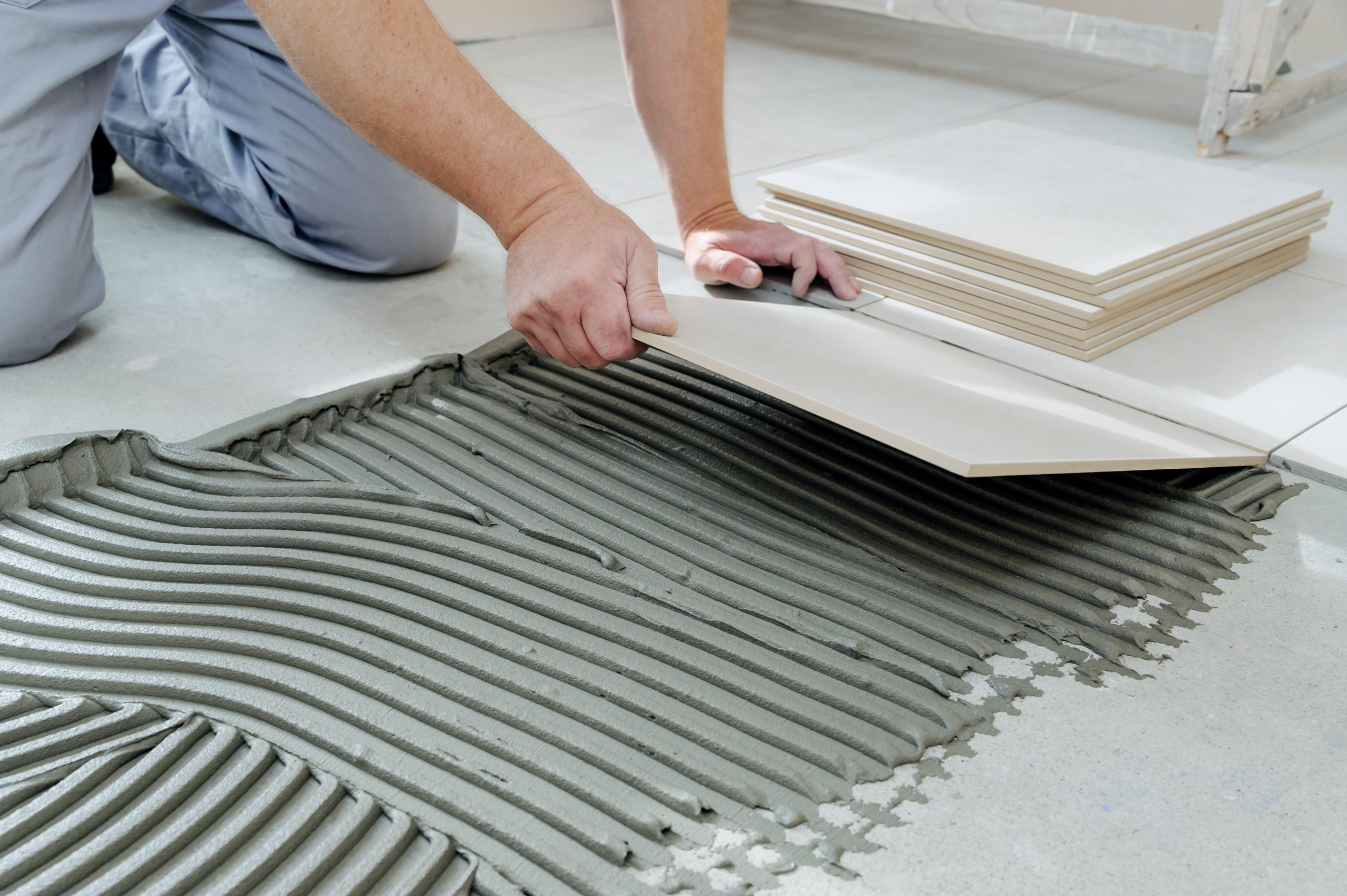  A professional flooring installer is installing laminate flooring in a new home. The installer is using a special saw to cut the laminate flooring to size. The installer is wearing safety glasses and a dust mask. The laminate flooring is a light brown color and has a wood grain pattern. The flooring is being installed in a living room.